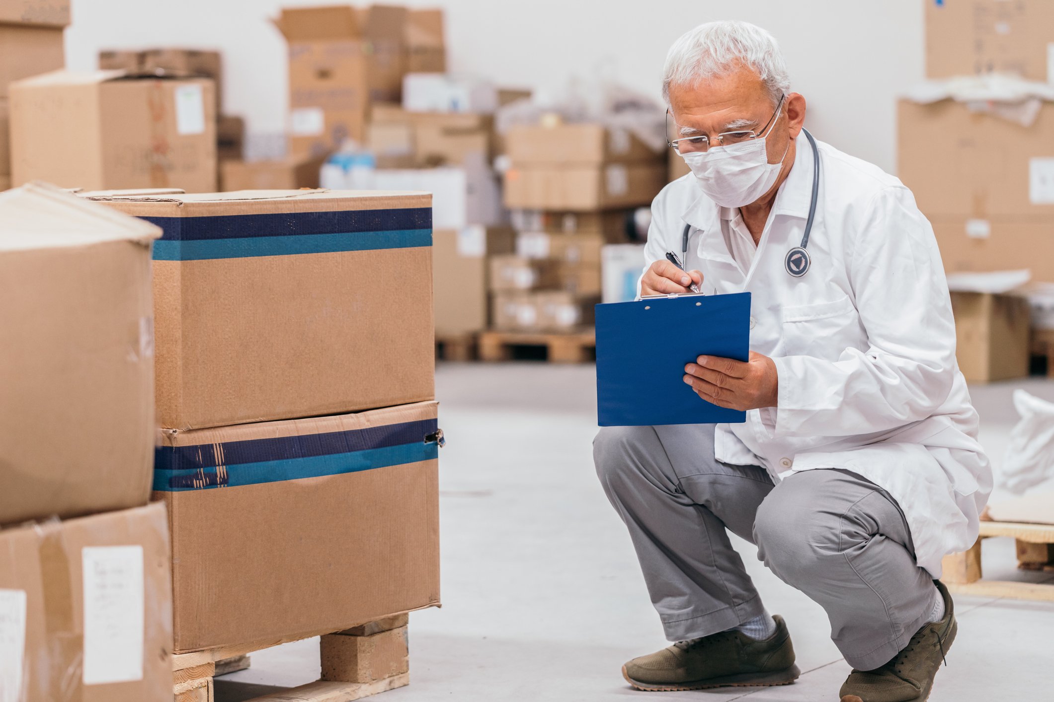 medical professional examining a checklist while crouched down and looking at boxes of stored medical equipment