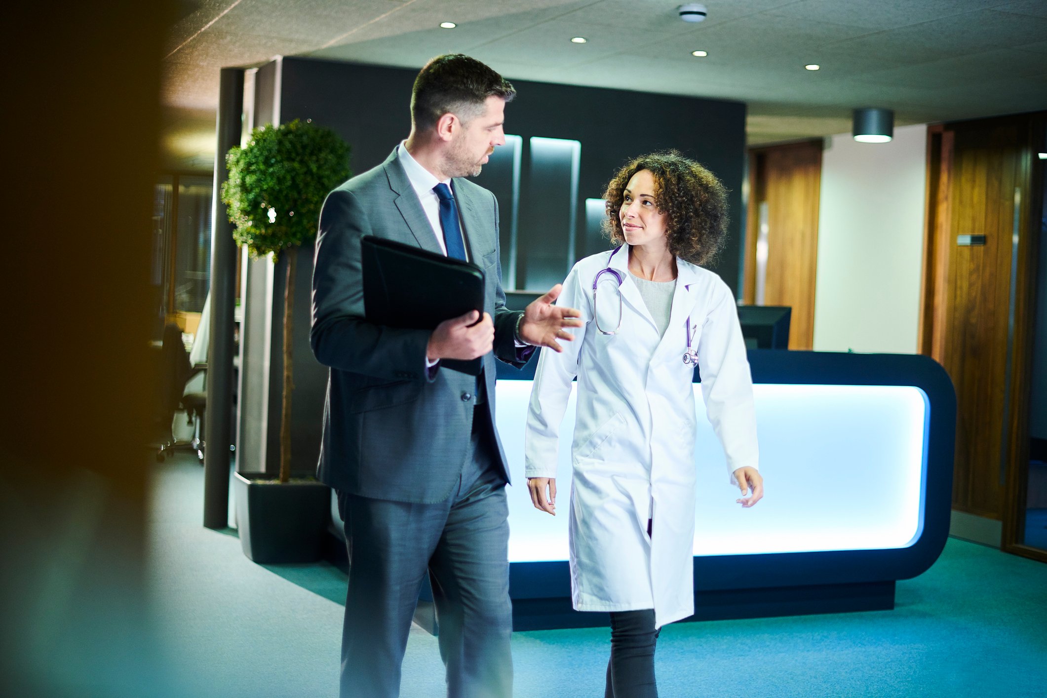 a businessman chats with a female doctor as they leave a boardroom meeting in a hospital