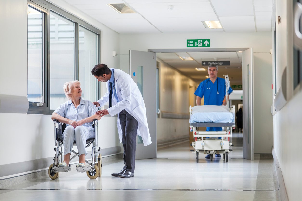 doctor with senior patient who is in a wheelchair inside of the hospital corridor